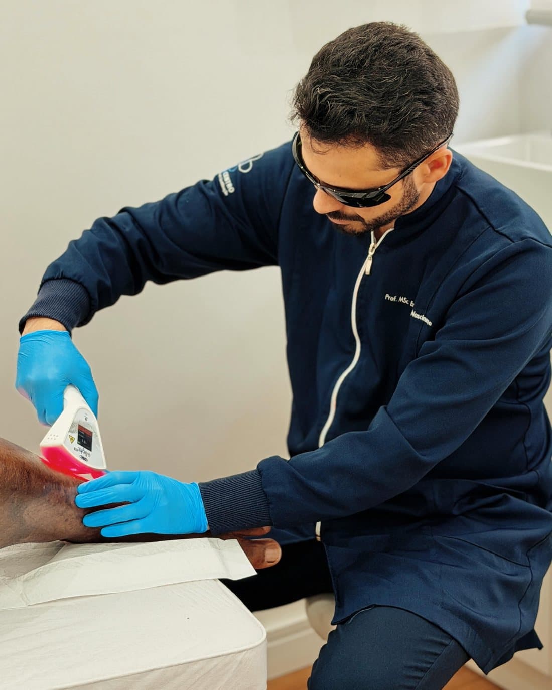 Profissional da Cicatricentro, com óculos de proteção, aplicando laserterapia na perna de um paciente